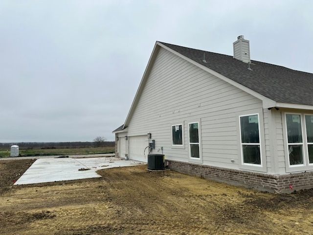 back of property with central AC unit and a garage