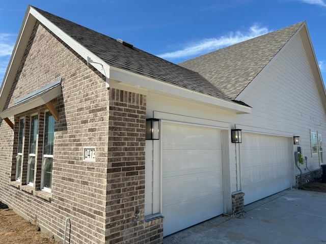 view of side of home with a shingled roof, concrete driveway, brick siding, and a garage