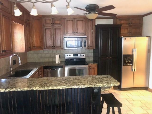 kitchen with appliances with stainless steel finishes, sink, backsplash, a kitchen bar, and kitchen peninsula