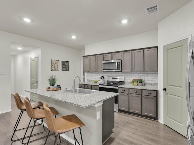 kitchen with sink, a breakfast bar area, stainless steel appliances, light stone countertops, and a center island with sink