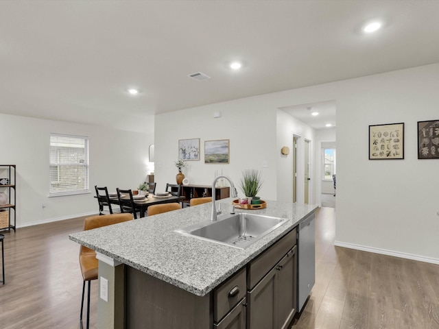 kitchen featuring dishwasher, an island with sink, sink, light stone counters, and plenty of natural light