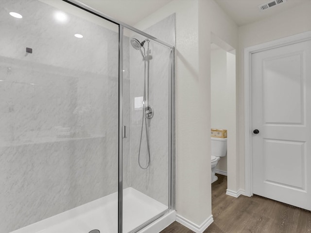 bathroom featuring a shower with shower door, hardwood / wood-style floors, and toilet