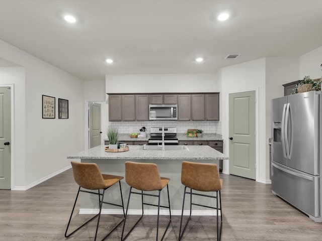 kitchen featuring light stone counters, light wood-type flooring, an island with sink, and appliances with stainless steel finishes