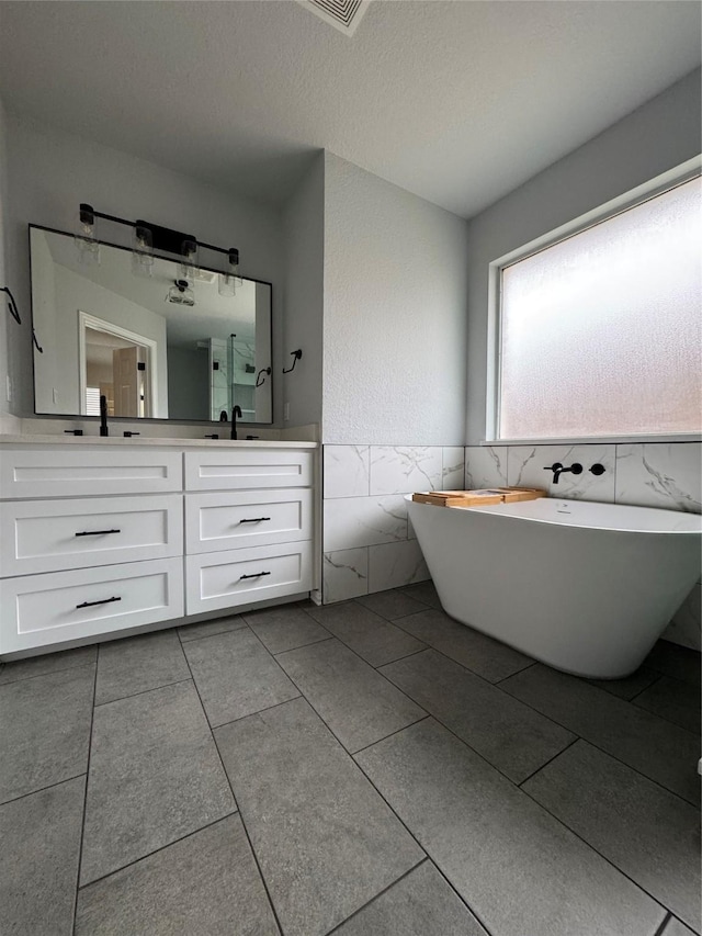 bathroom featuring tile walls, tile patterned flooring, vanity, a bath, and a textured ceiling