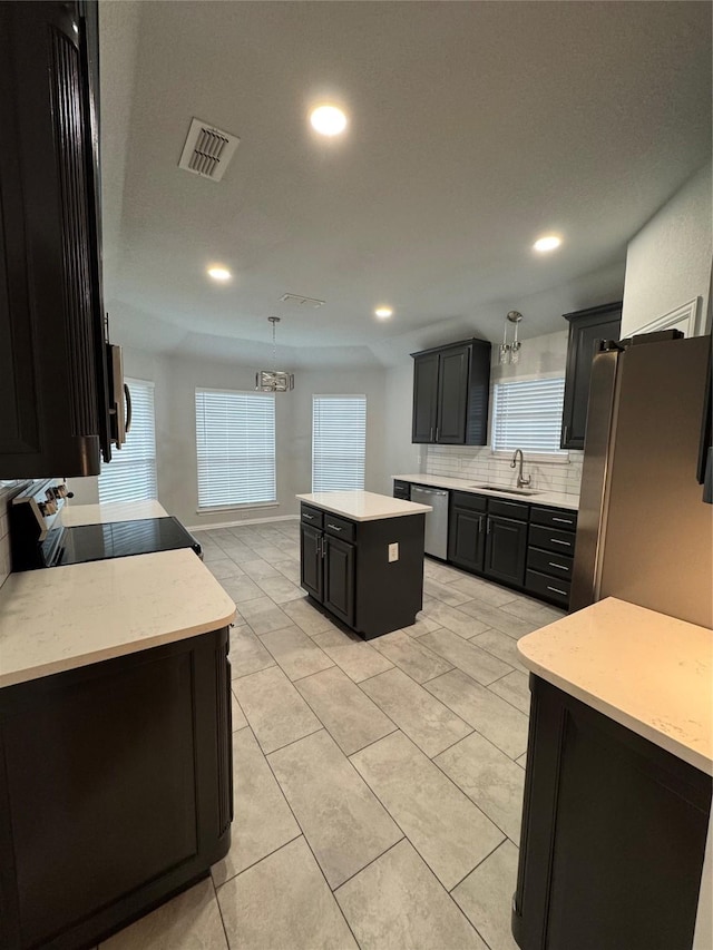 kitchen featuring sink, appliances with stainless steel finishes, a center island, tasteful backsplash, and decorative light fixtures