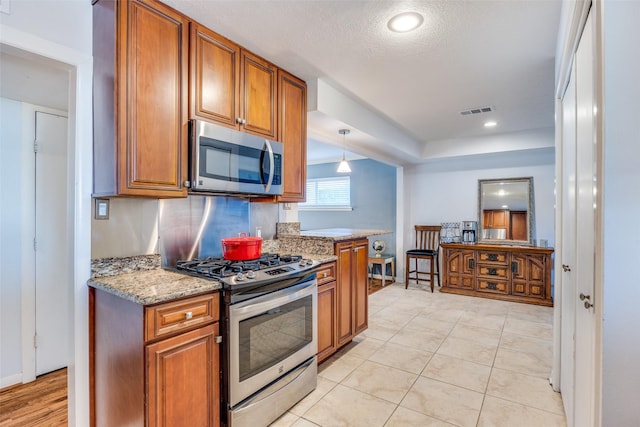 kitchen with light tile patterned flooring, light stone counters, hanging light fixtures, a textured ceiling, and appliances with stainless steel finishes