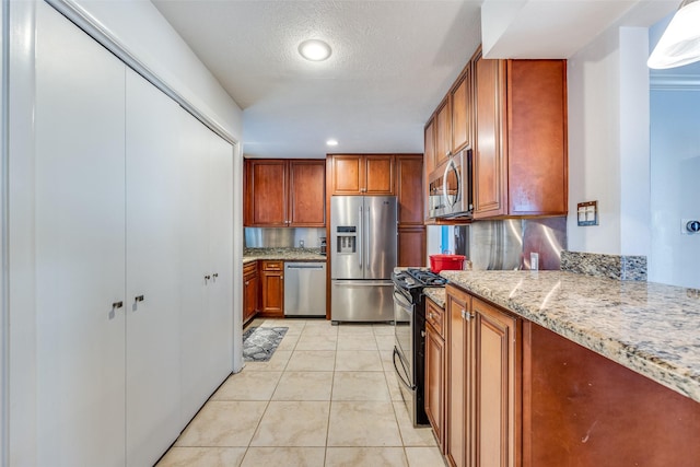 kitchen featuring light stone countertops, light tile patterned floors, stainless steel appliances, and a textured ceiling