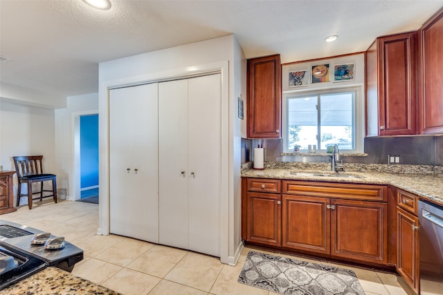 kitchen featuring light stone counters, stainless steel dishwasher, sink, and light tile patterned floors