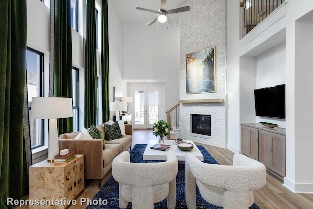 living room with a brick fireplace, light hardwood / wood-style floors, ceiling fan, and a high ceiling