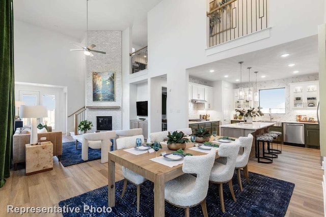 dining space with a brick fireplace, a towering ceiling, and light hardwood / wood-style flooring