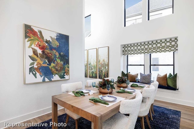 dining area with hardwood / wood-style floors, a healthy amount of sunlight, and a high ceiling