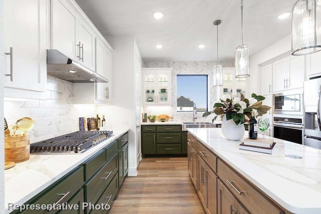 kitchen with appliances with stainless steel finishes, decorative light fixtures, sink, white cabinets, and light wood-type flooring