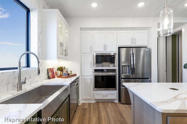 kitchen featuring decorative light fixtures, white cabinetry, sink, light stone counters, and stainless steel appliances