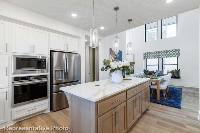 kitchen with white cabinetry, stainless steel appliances, light stone counters, a kitchen island, and decorative light fixtures