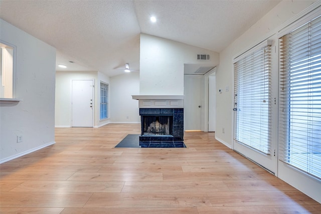 unfurnished living room featuring lofted ceiling, a tiled fireplace, light hardwood / wood-style floors, and a textured ceiling