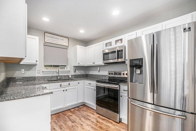 kitchen with white cabinetry, sink, dark stone counters, stainless steel appliances, and light hardwood / wood-style flooring