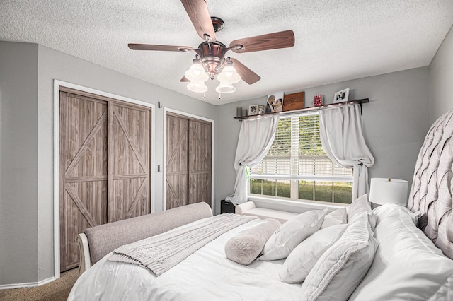 carpeted bedroom featuring multiple closets, ceiling fan, and a textured ceiling