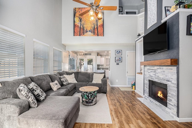 living room with ceiling fan, wood-type flooring, a stone fireplace, and a high ceiling