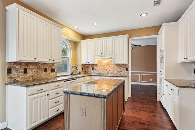 kitchen with white cabinets, dark hardwood / wood-style flooring, dark stone counters, a center island, and white appliances