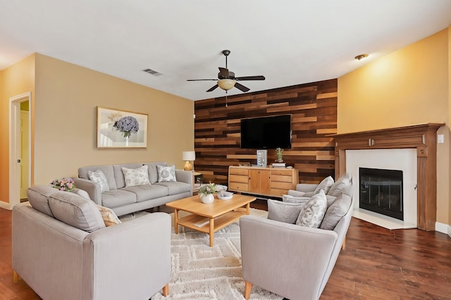 living room featuring an accent wall, wood walls, visible vents, a ceiling fan, and dark wood-style flooring