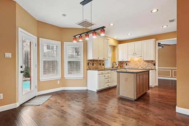 kitchen featuring a center island, hanging light fixtures, white dishwasher, dark stone counters, and backsplash