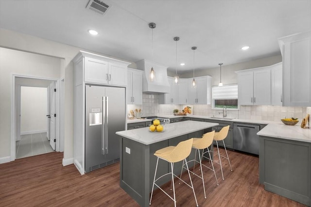 kitchen with pendant lighting, sink, white cabinetry, stainless steel appliances, and a kitchen island