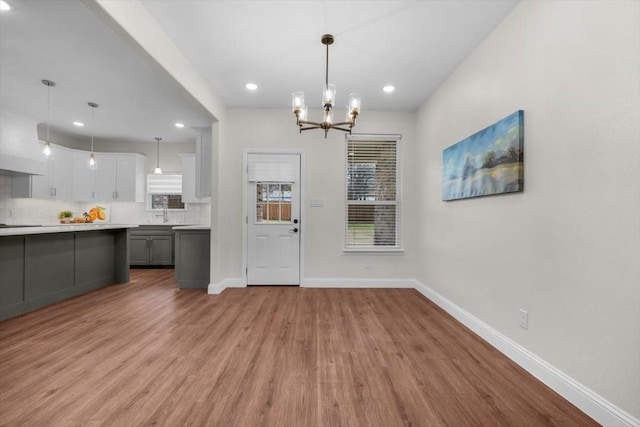 unfurnished dining area featuring an inviting chandelier, sink, and light hardwood / wood-style flooring