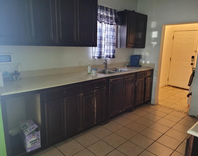 kitchen featuring light tile patterned floors, white microwave, light countertops, dark brown cabinets, and a sink