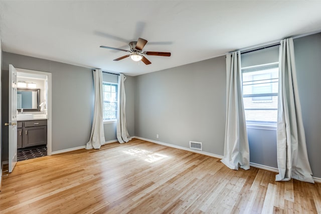 unfurnished bedroom with ensuite bathroom, ceiling fan, and light wood-type flooring