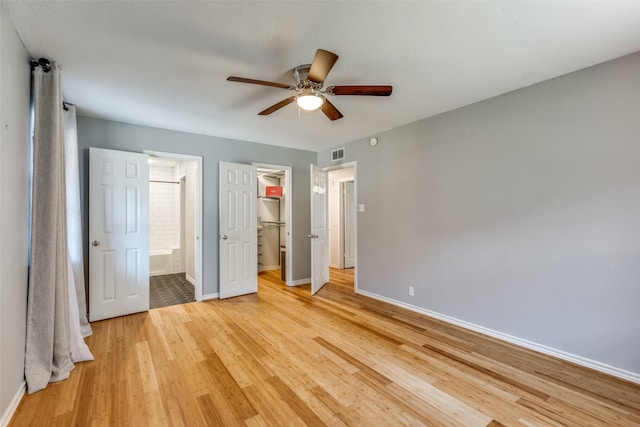 unfurnished bedroom with hardwood / wood-style flooring, ceiling fan, connected bathroom, a walk in closet, and a closet