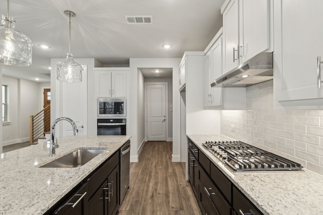 kitchen with sink, stainless steel appliances, light stone counters, white cabinets, and decorative light fixtures