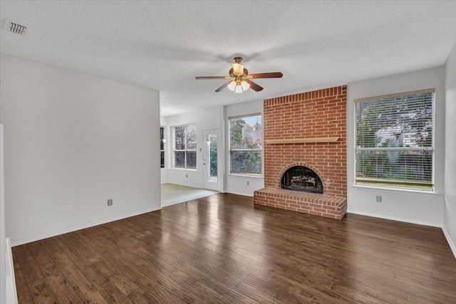 unfurnished living room featuring ceiling fan, a brick fireplace, dark hardwood / wood-style floors, and a textured ceiling