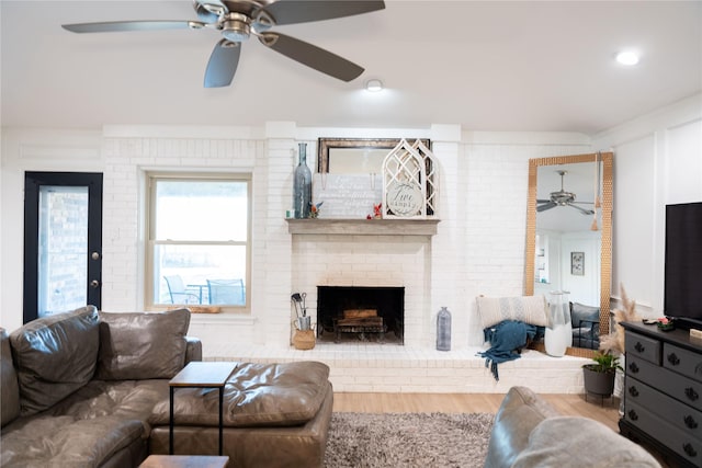 living room with a brick fireplace, wood-type flooring, ornamental molding, and brick wall