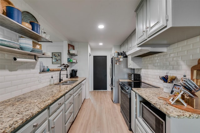 kitchen with built in microwave, sink, light stone counters, light hardwood / wood-style floors, and black / electric stove