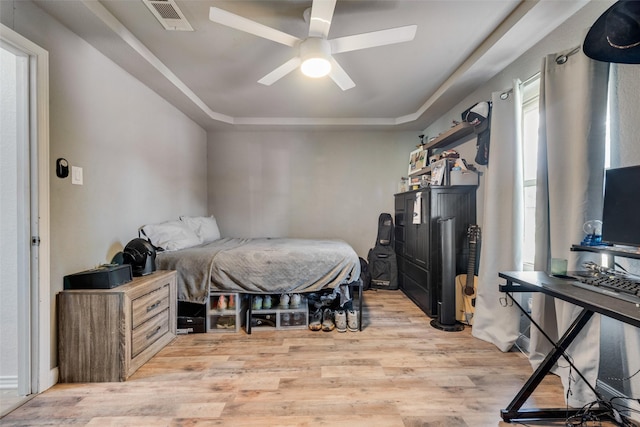 bedroom with light hardwood / wood-style flooring, ceiling fan, and a tray ceiling