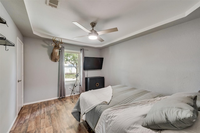 bedroom with a tray ceiling, wood-type flooring, and ceiling fan