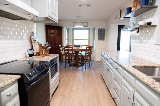 kitchen with black range with electric cooktop, custom range hood, light stone countertops, light hardwood / wood-style floors, and white cabinets