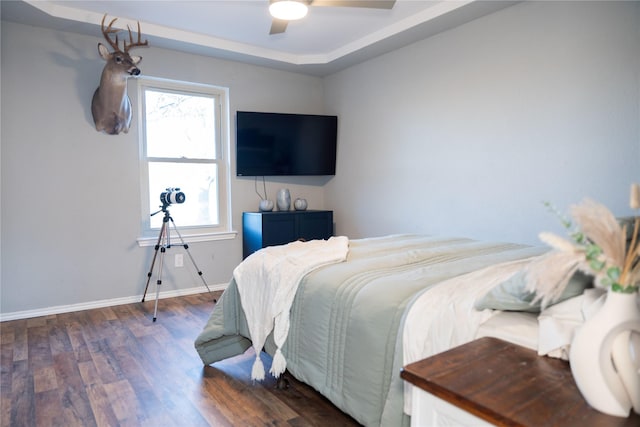 bedroom with a raised ceiling, dark wood-type flooring, and ceiling fan