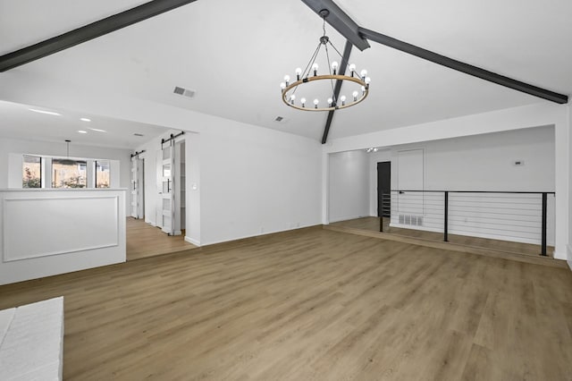 unfurnished living room with an inviting chandelier, hardwood / wood-style floors, beam ceiling, high vaulted ceiling, and a barn door