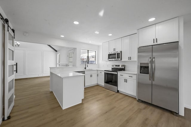 kitchen with white cabinetry, sink, kitchen peninsula, stainless steel appliances, and a barn door