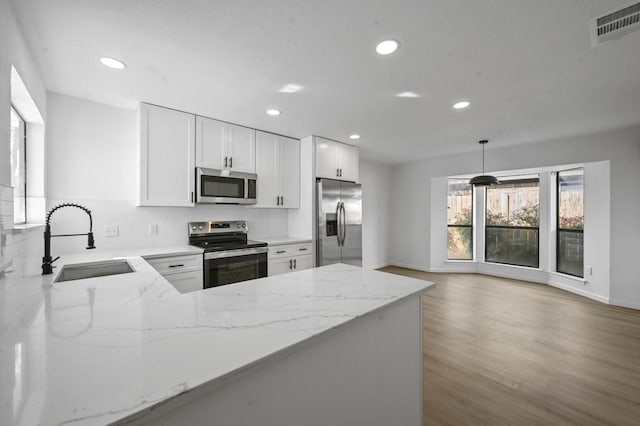 kitchen with sink, hanging light fixtures, kitchen peninsula, stainless steel appliances, and white cabinets