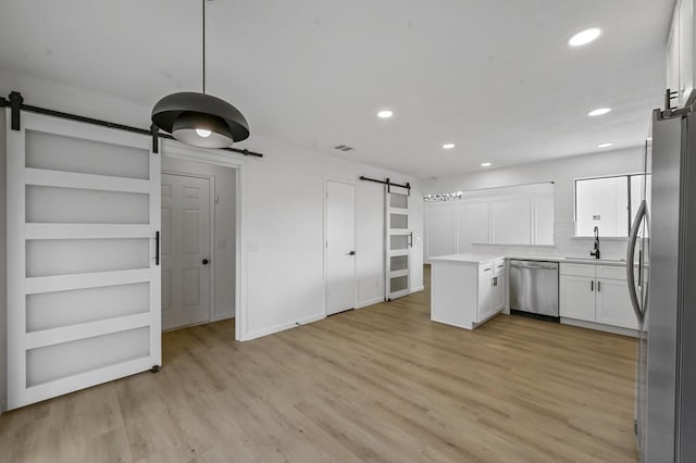 kitchen with sink, white cabinetry, stainless steel appliances, light hardwood / wood-style floors, and a barn door