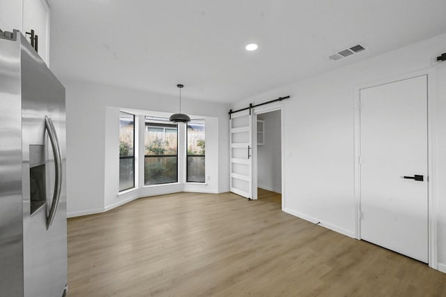 kitchen featuring white cabinetry, light hardwood / wood-style flooring, stainless steel fridge, pendant lighting, and a barn door