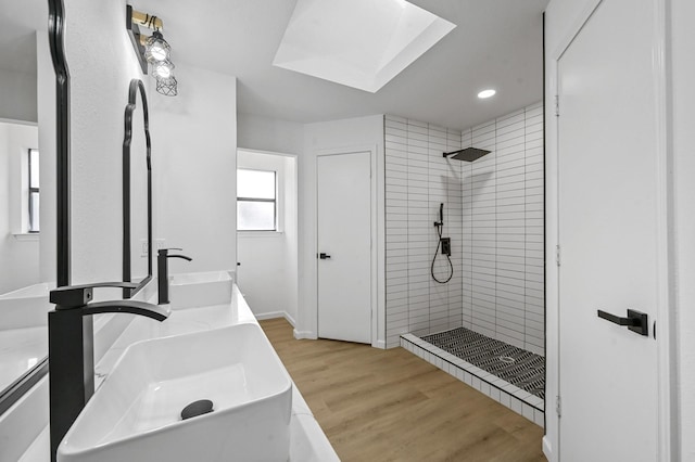 bathroom with a tile shower, hardwood / wood-style floors, vanity, and a skylight