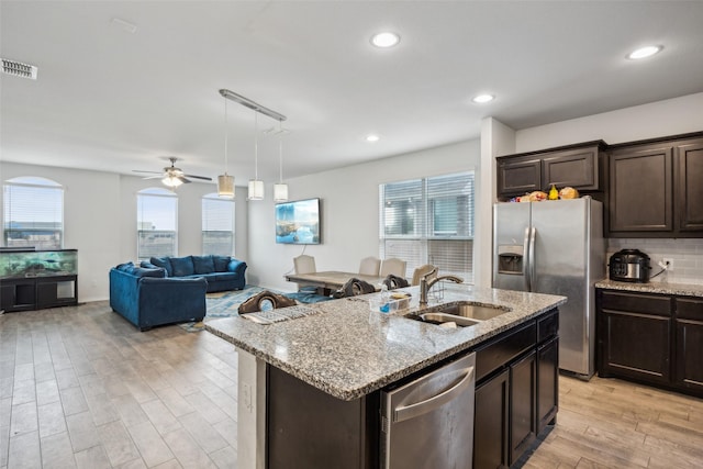 kitchen featuring appliances with stainless steel finishes, decorative light fixtures, an island with sink, sink, and light hardwood / wood-style floors