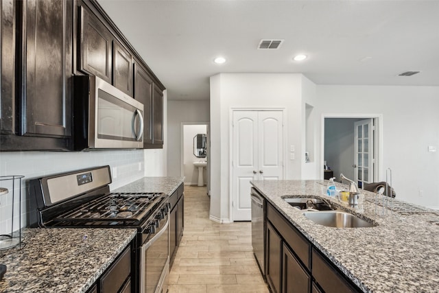 kitchen featuring sink, decorative backsplash, dark stone counters, stainless steel appliances, and light hardwood / wood-style flooring