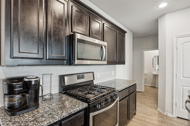 kitchen with dark brown cabinetry, dark stone countertops, stainless steel appliances, light hardwood / wood-style floors, and decorative backsplash