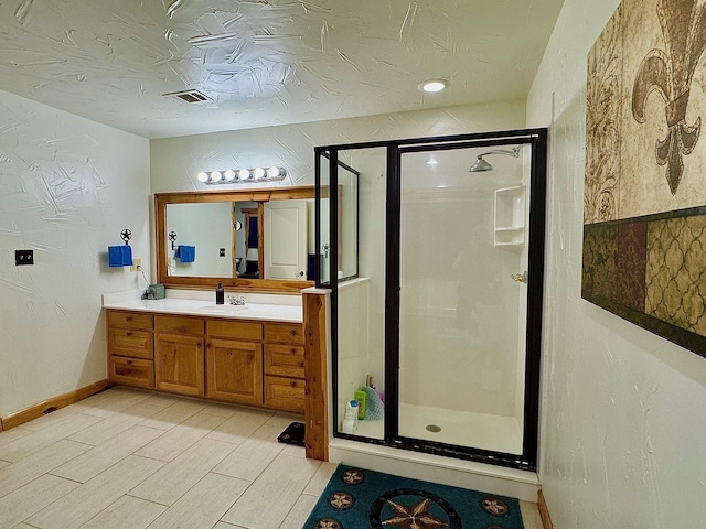 bathroom with vanity, a shower with shower door, and a textured ceiling