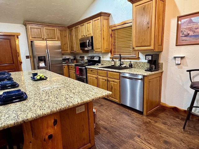 kitchen with dark hardwood / wood-style floors, lofted ceiling, sink, light stone counters, and stainless steel appliances