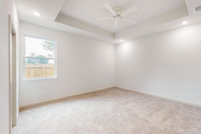 empty room with visible vents, a ceiling fan, light colored carpet, a tray ceiling, and recessed lighting